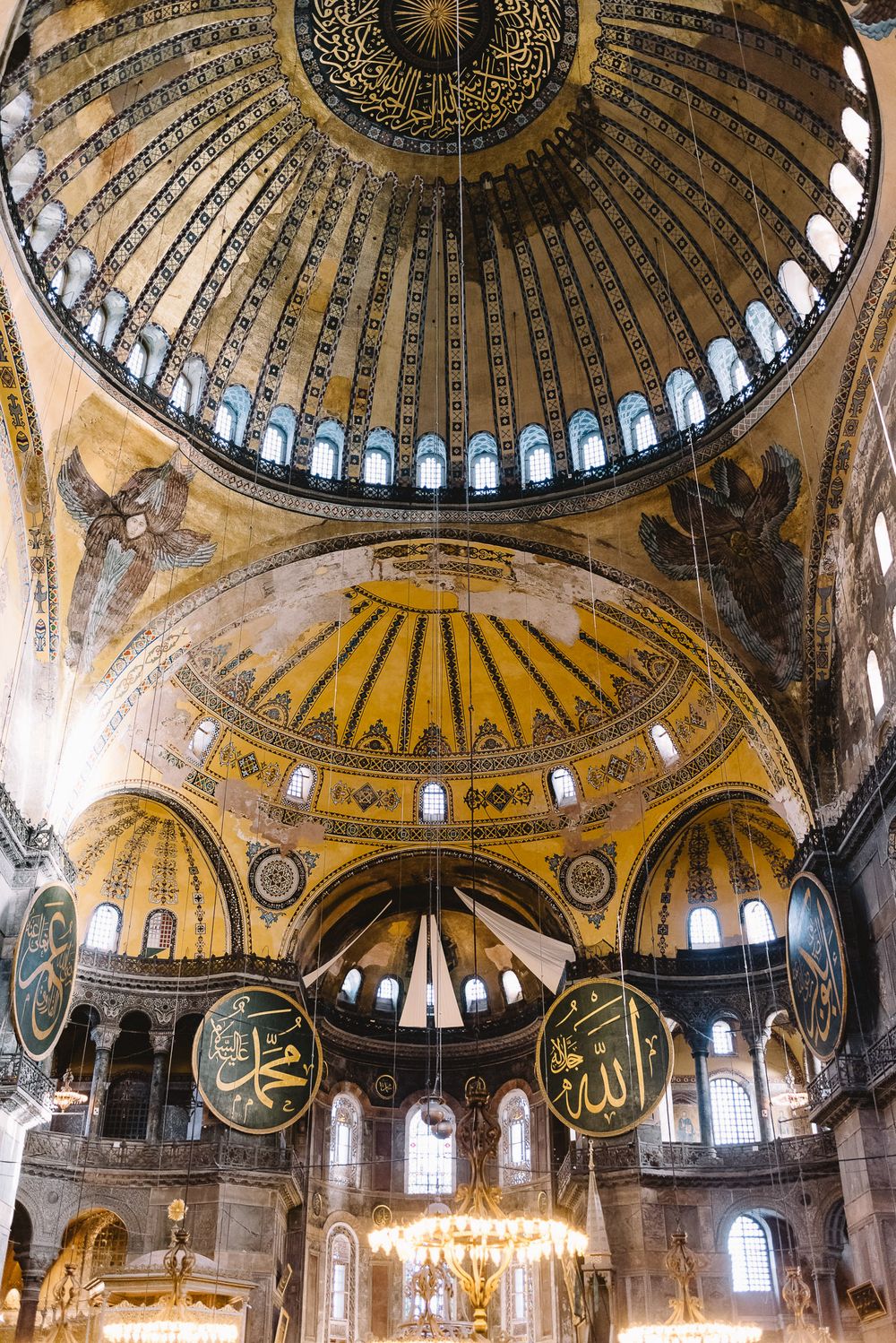 Interior of Hagia Sophia featuring grand Byzantine dome, Islamic calligraphy medallions, and golden mosaics in Istanbul.