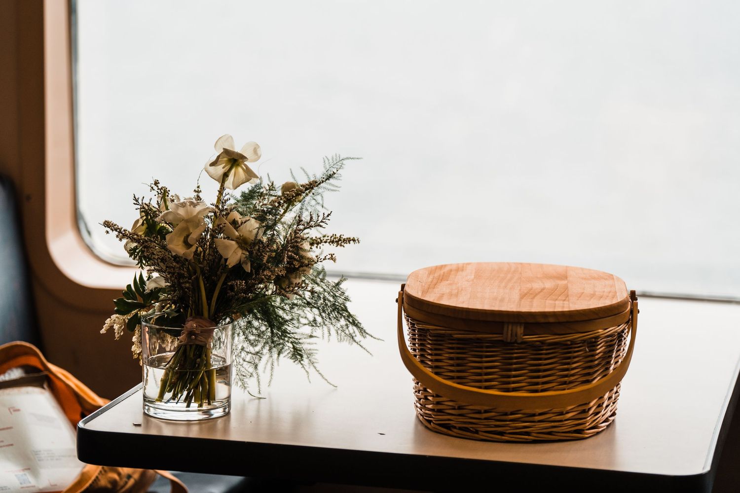 Rustic wedding bouquet in glass vase beside wicker basket on ferry table. Bainbridge island ferry elopement