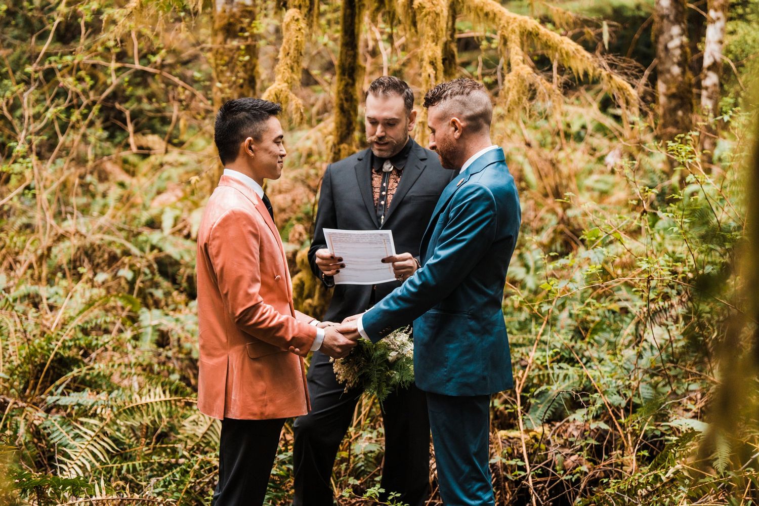 Two grooms exchanging vows in lush forest ceremony with officiant. Bainbridge island ferry elopement
