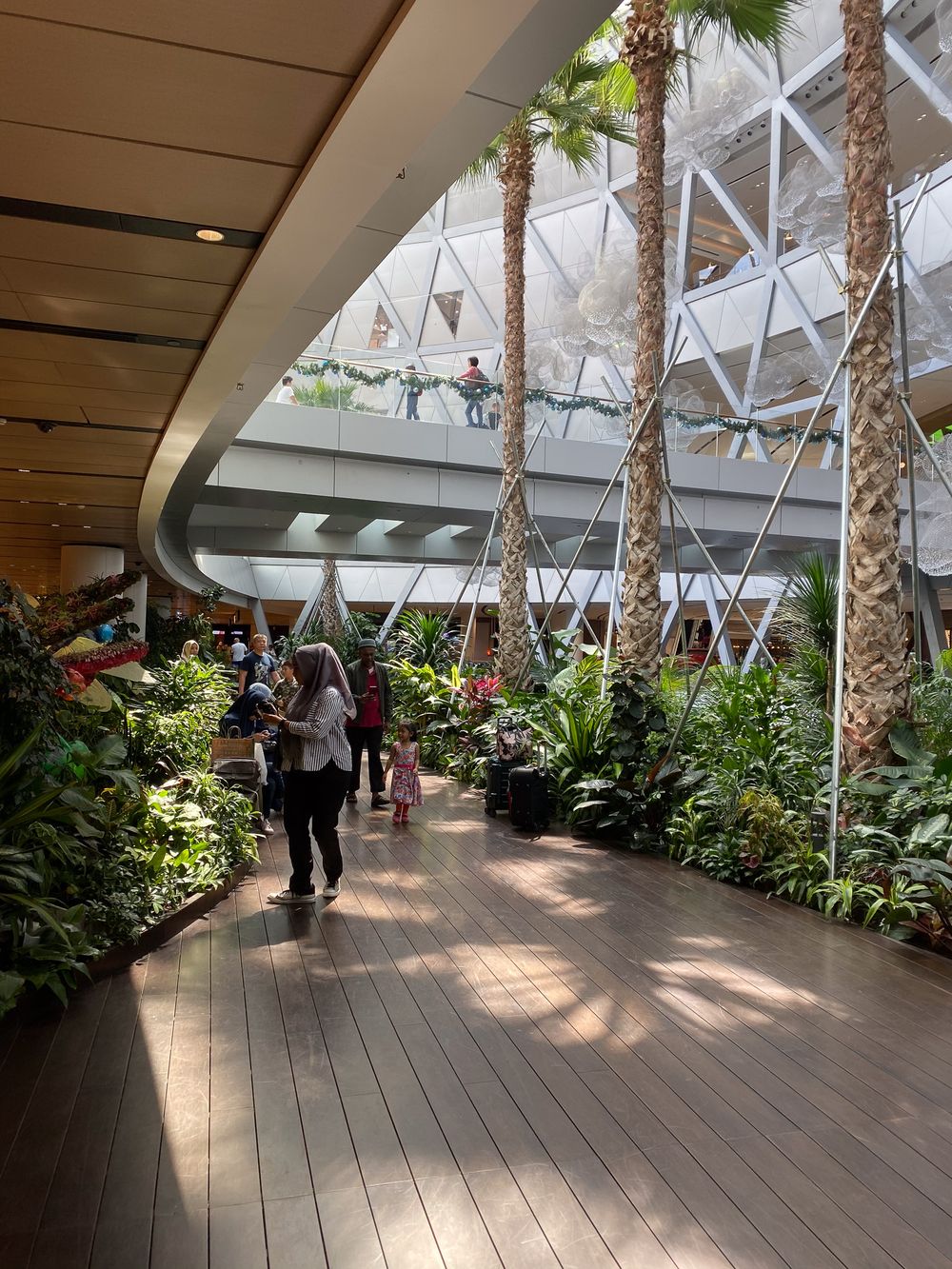 Changi Jewel, Singapore. Lush tropical garden walkway inside a modern mall with palm trees and green plants.