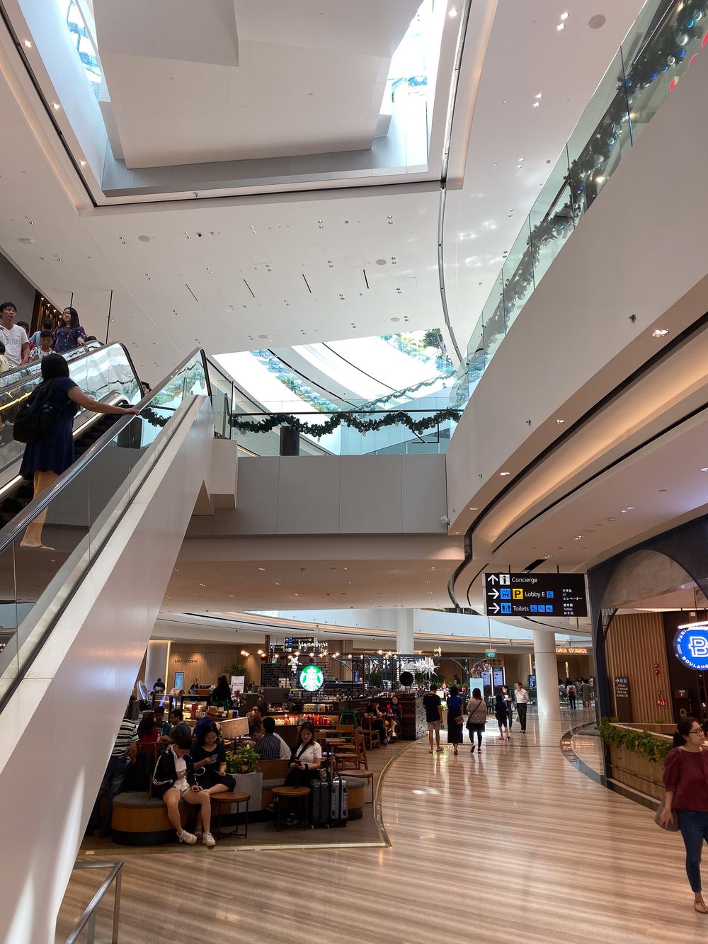 Changi Jewel, Singapore. Multi-level modern shopping mall interior with escalators, Starbucks cafe, and bright natural lighting.