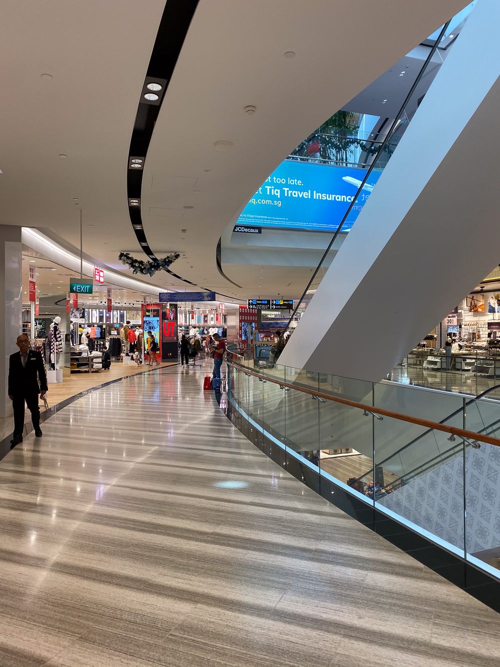 Changi Jewel, Singapore. Busy airport terminal corridor with travel insurance advertisement screen and retail shops.