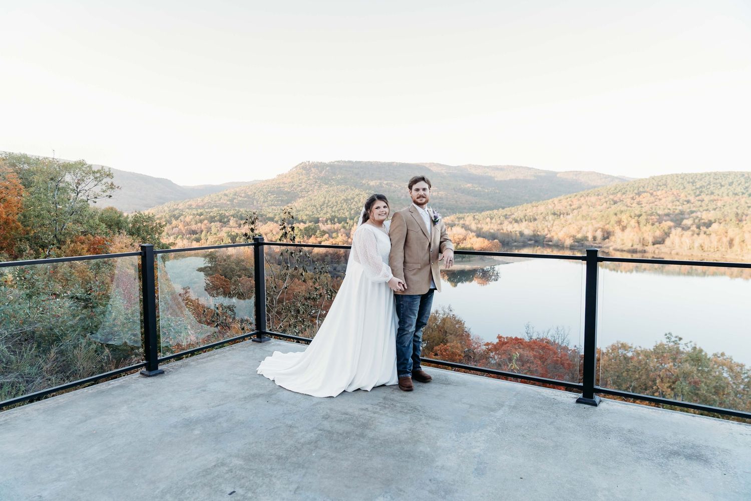 Wedding couple stands on wooden bridge over reflective pond during overcast day. Toupon Lodge Wedding Venue in Deville, La