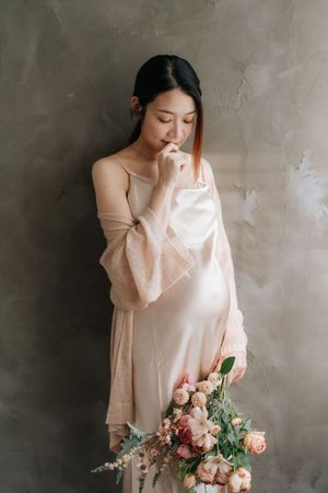 A figure in a soft cream sweater holds a romantic bouquet of pink and peach roses against a textured gray wall.一位身穿淺奶油色毛衣的女子手捧一束浪漫的粉紅色和桃色玫瑰