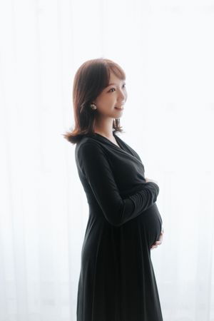 Silhouette of pregnant woman in black dress against white backdrop shown in three different poses一位身穿黑色連身裙的孕婦在白色背景前擺出三種不同的姿勢，構成剪影。