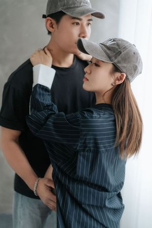 A couple in baseball caps and casual attire share intimate moments in a series of romantic poses against a gray backdrop.一對戴著棒球帽、穿著休閒裝的情侶在灰色