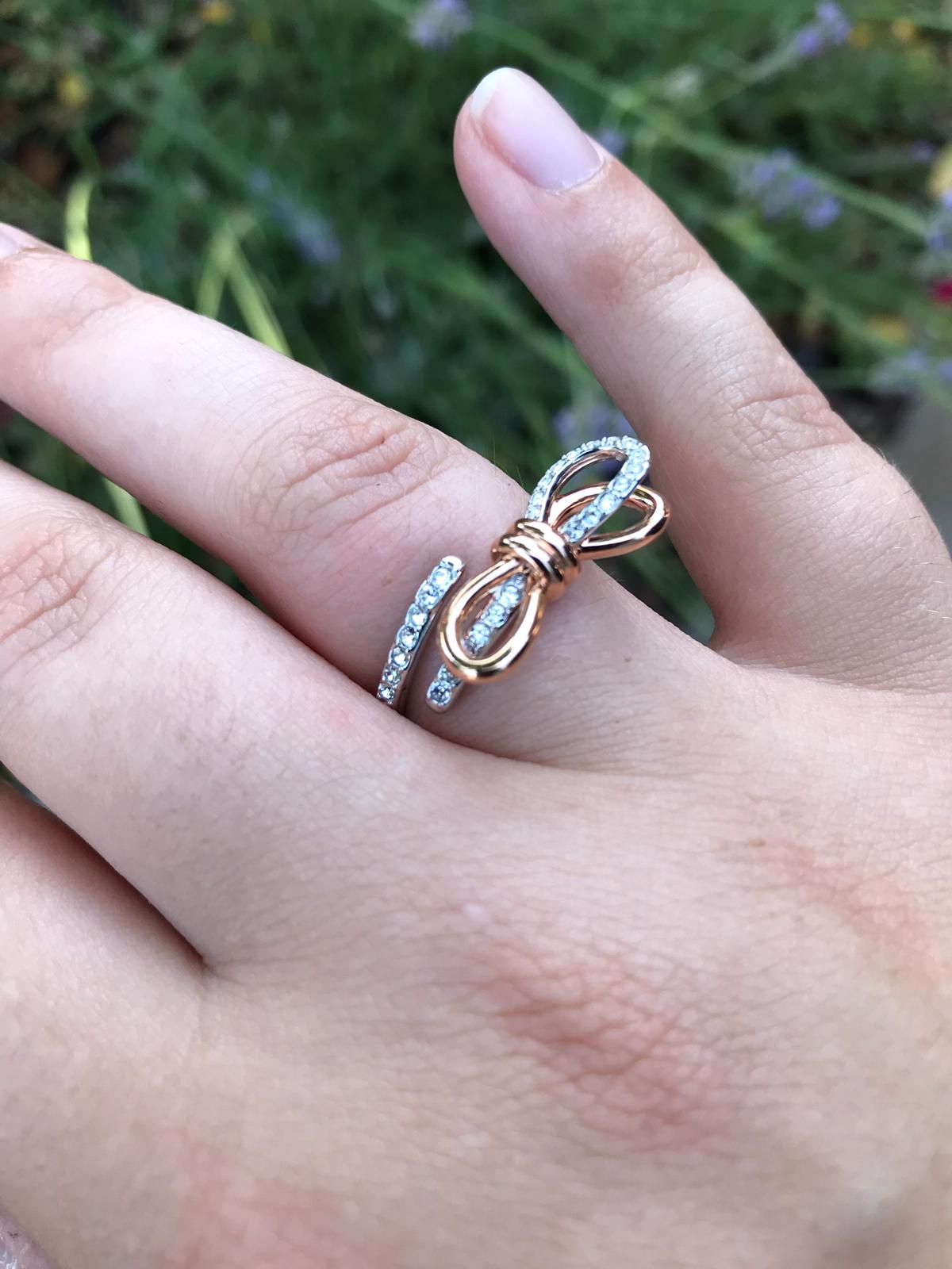 Een elegante roségouden ring met een strik, bezet met fonkelende diamanten, wordt buiten aan de hand van een vrouw getoond.
