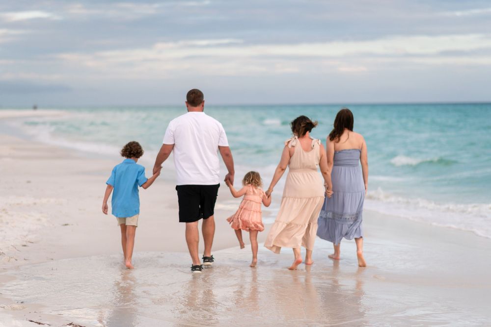 Family of five walking hand-in-hand along a white sandy beach with turquoise ocean waves in the background.