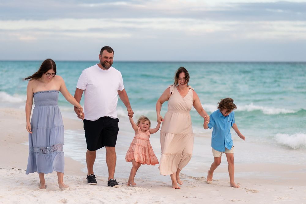 Family of five walking hand-in-hand on a white sand beach, with turquoise ocean waves in the background.