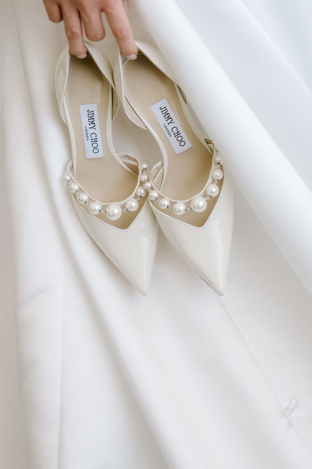Jimmy Choo white pearl embellished pointed-toe flats displayed against a bridal gown.