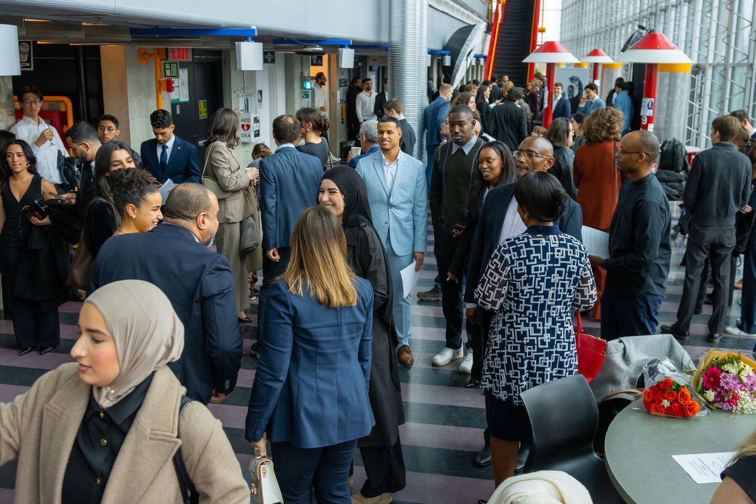 Diverse professionals networking at a formal indoor event, mingling in a modern venue with colorful decor.