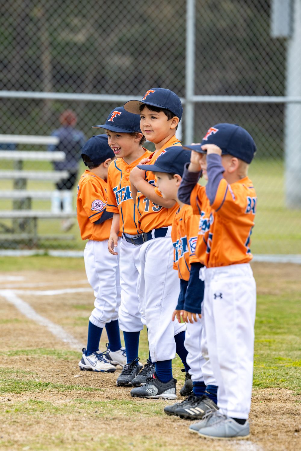 A group of young baseball players in orange and navy uniforms line up together on the field during a game.