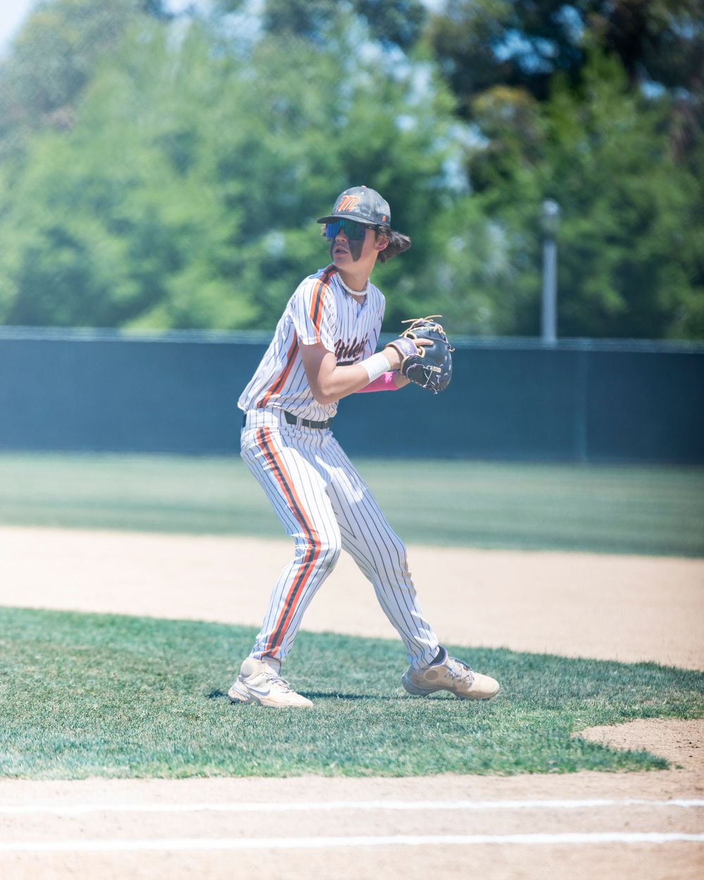 Irvine baseball game a young baseball player in pinstripe uniform crouches in ready position at first base during a sunny outdoor game.
