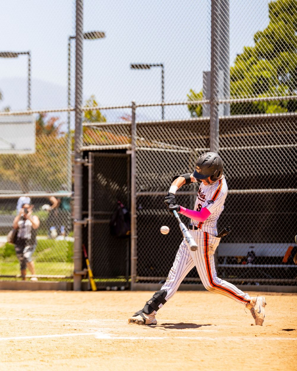 Irvine baseball game a youth baseball player in pinstripe uniform swings a pink bat at an incoming pitch during a sunny afternoon game.