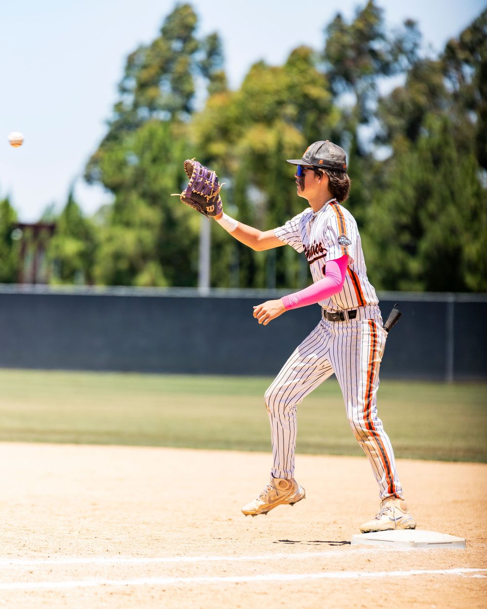 Irvine baseball game a young baseball player in pinstripe uniform catches a ball at first base during a sunny outdoor youth baseball game.