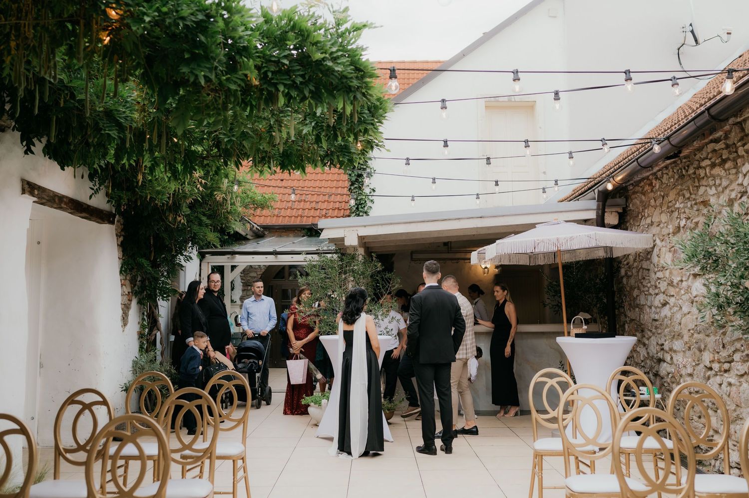 Guests mingling in a charming outdoor courtyard wedding venue with string lights and wicker chairs.