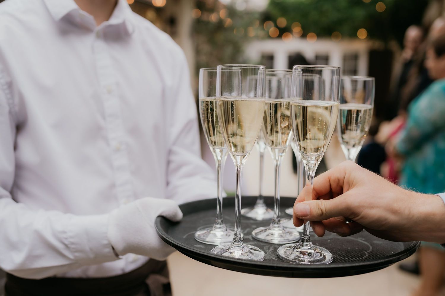 A waiter in white gloves serves champagne flutes on a tray at an elegant wedding reception.