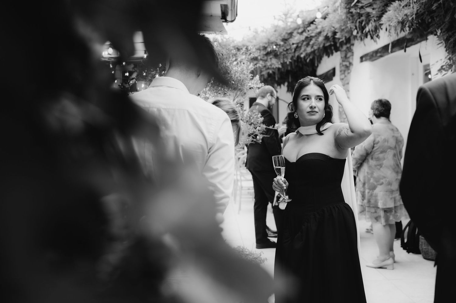 Black and white photo of a woman in a strapless black dress at an outdoor wedding reception.