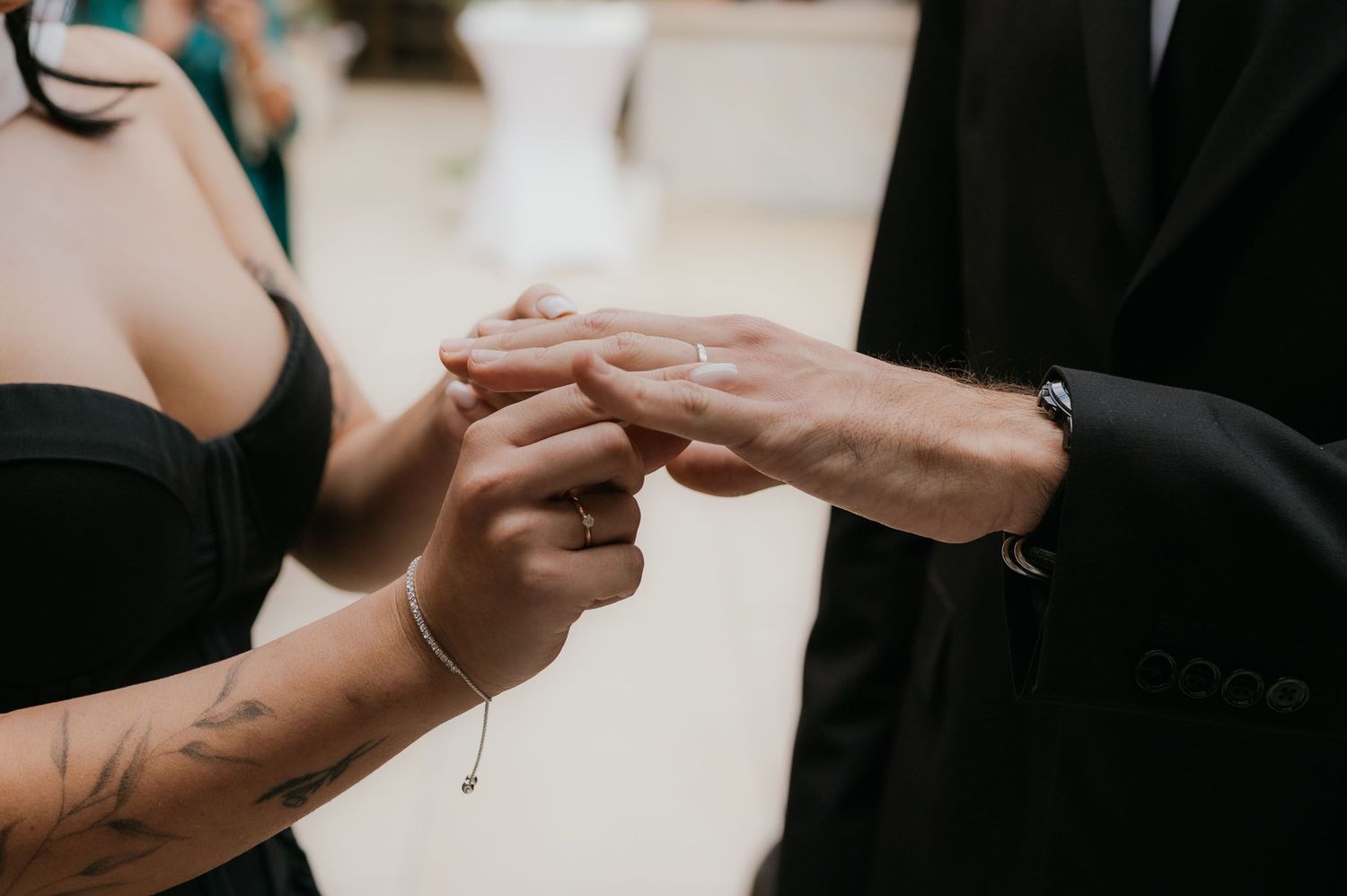 Close-up of a bride with tattoos placing a wedding ring on the grooms finger during ceremony.