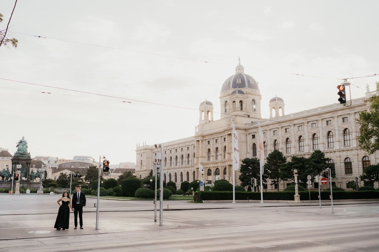 Couple in formal attire posing near Vienna's Natural History Museum on a quiet city street.