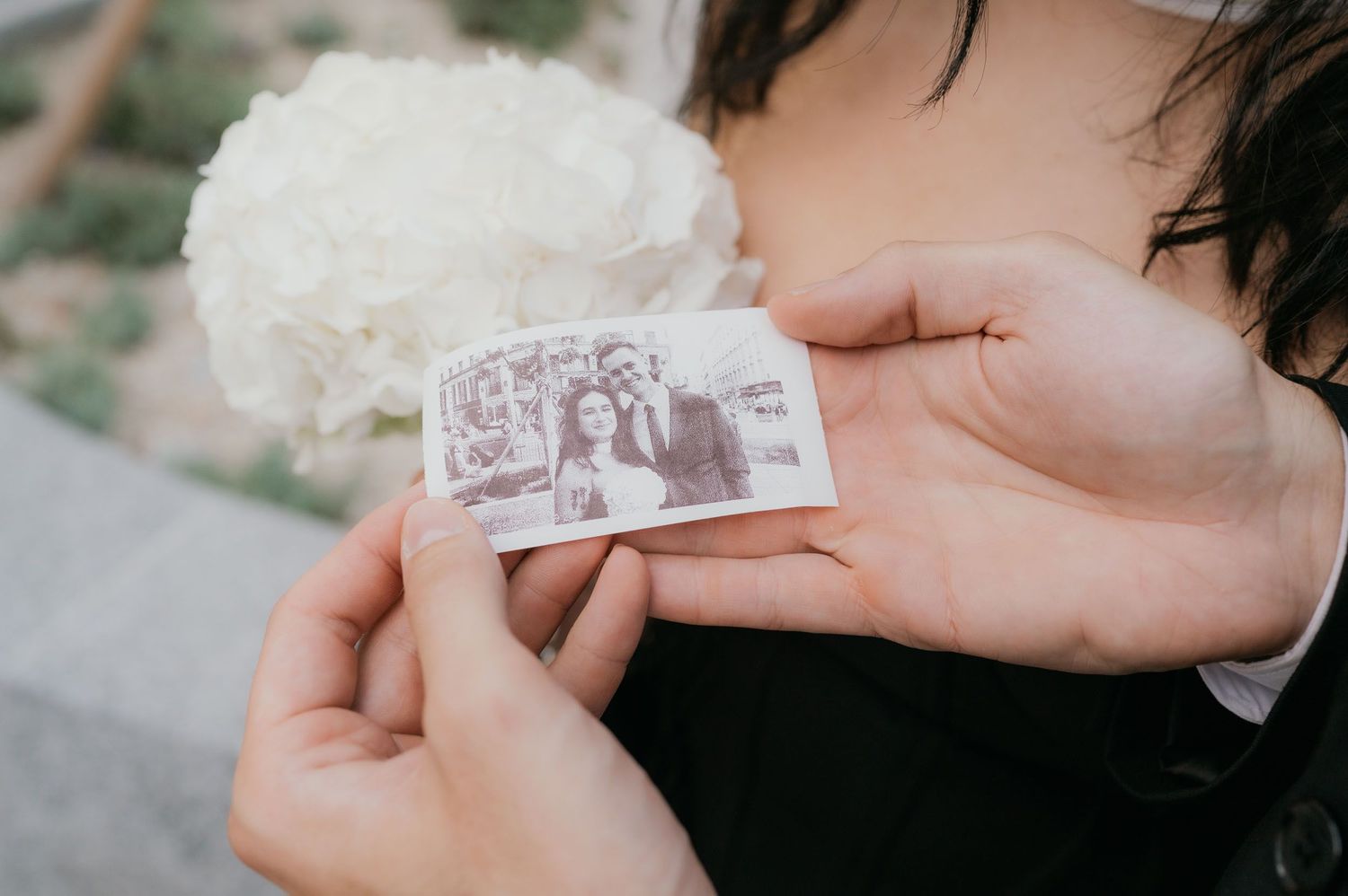 Couple holding a vintage black and white photo at their wedding, with a white floral bouquet in the background.