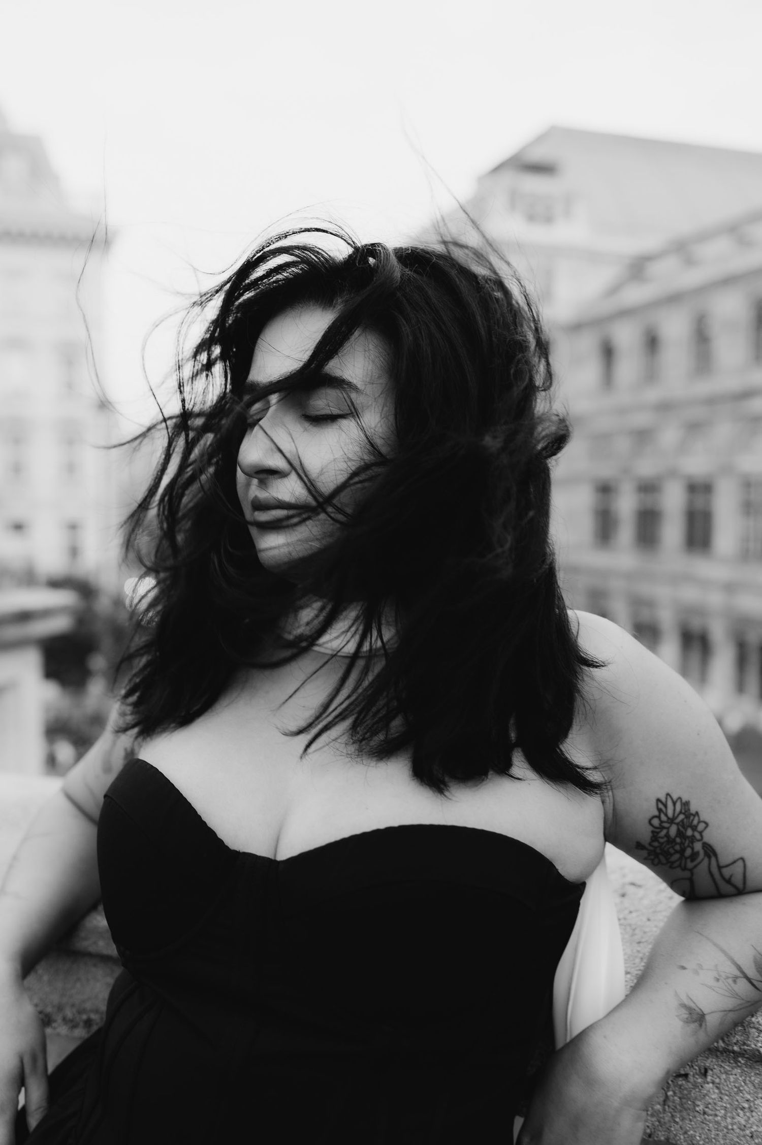 Black and white portrait of a woman with windswept hair wearing a strapless black dress outdoors.
