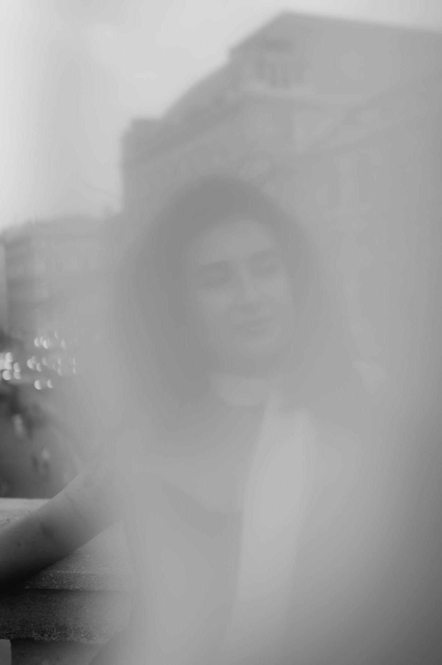 Blurry black and white portrait of a woman smiling outdoors near a building, captured through a dreamy, soft-focus lens.