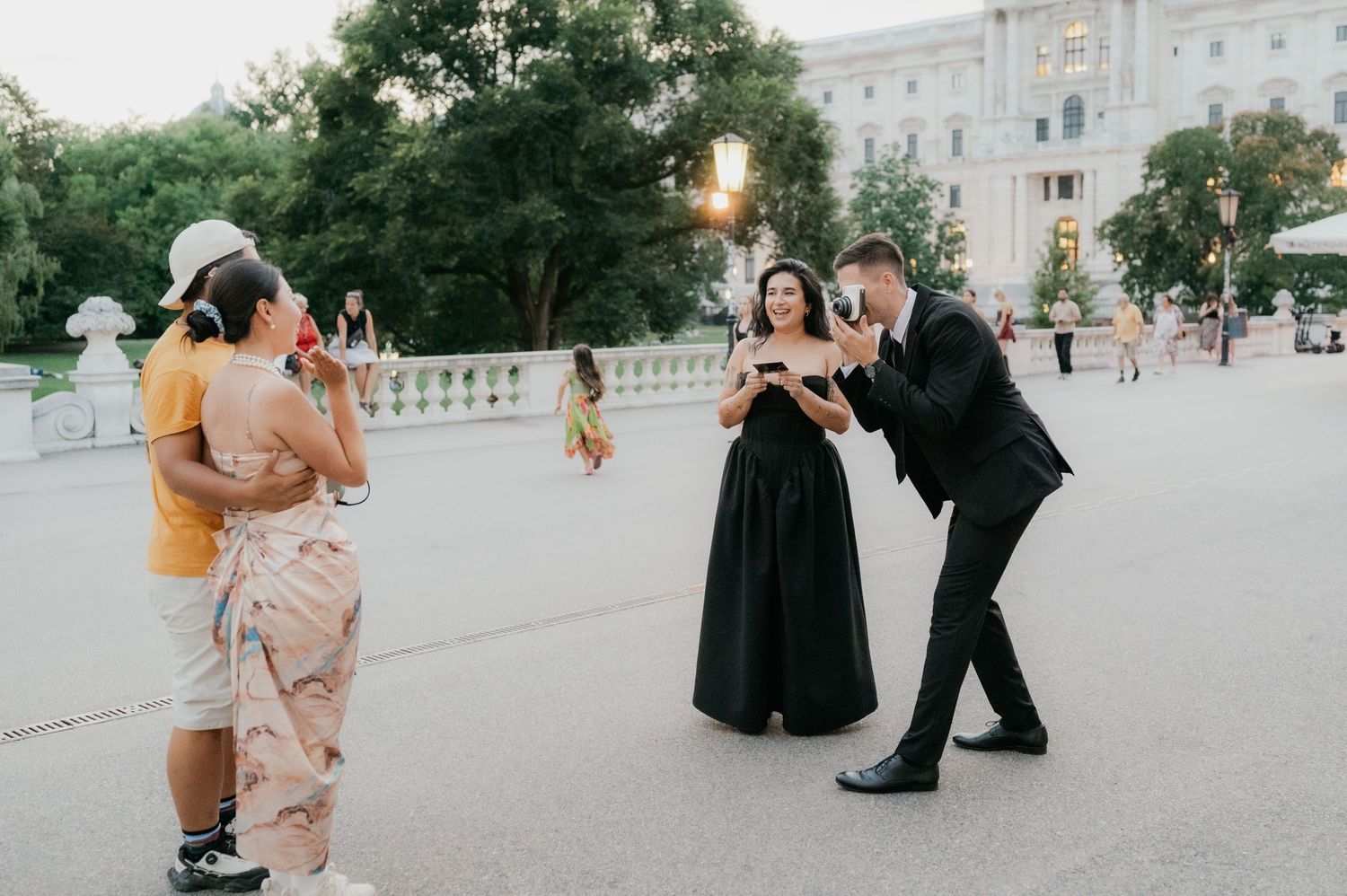 Couple in formal attire poses for photos outdoors near elegant white building at golden hour.