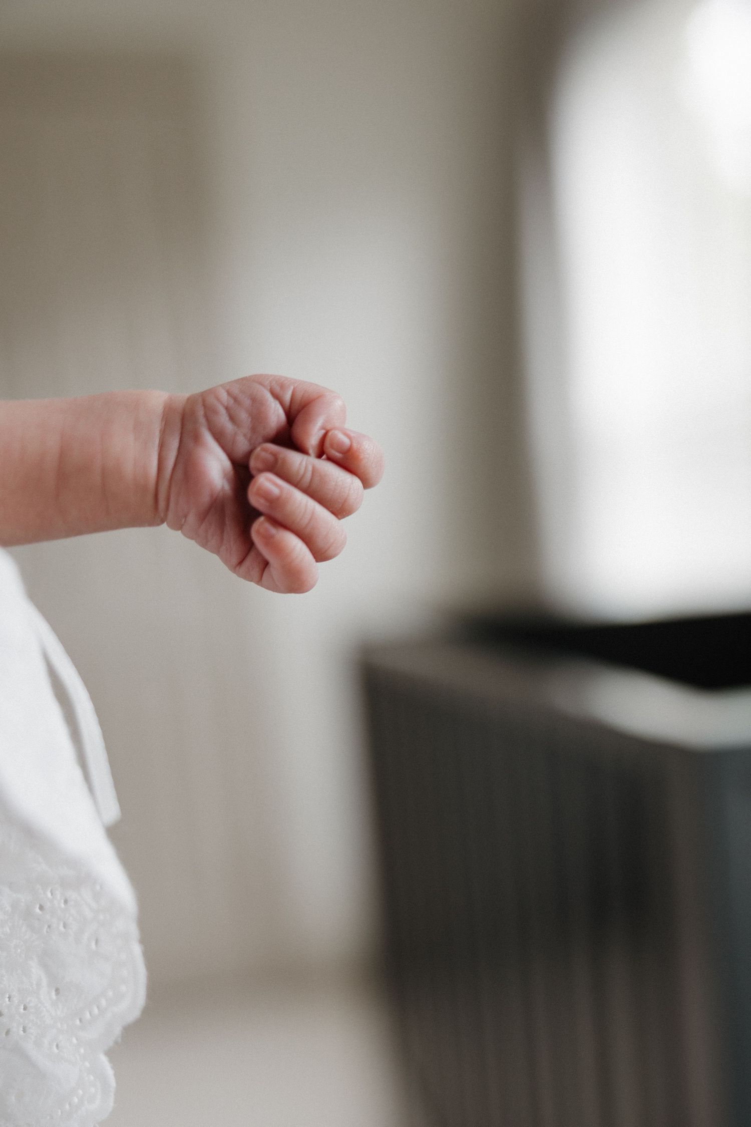 Close-up of a newborn baby's tiny clenched fist against a soft white cloth in a bright, airy room.