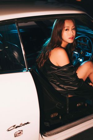 Young woman in black leather dress poses inside a vintage white Camaro at night with blue neon lighting.