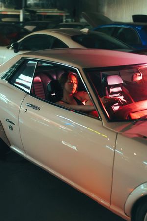 Woman sitting in a classic white Cobra muscle car with red interior lighting in a parking garage.
