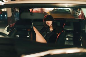 Young woman sitting in the backseat of a vintage car viewed through rear window.