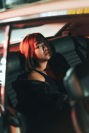 Young woman with red hair sits in car interior illuminated by red neon light.