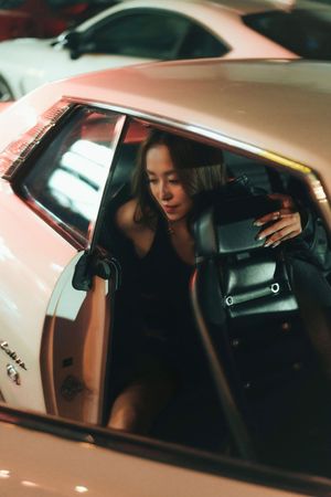 Young woman in black dress exiting a white Lamborghini at night, holding a black handbag.