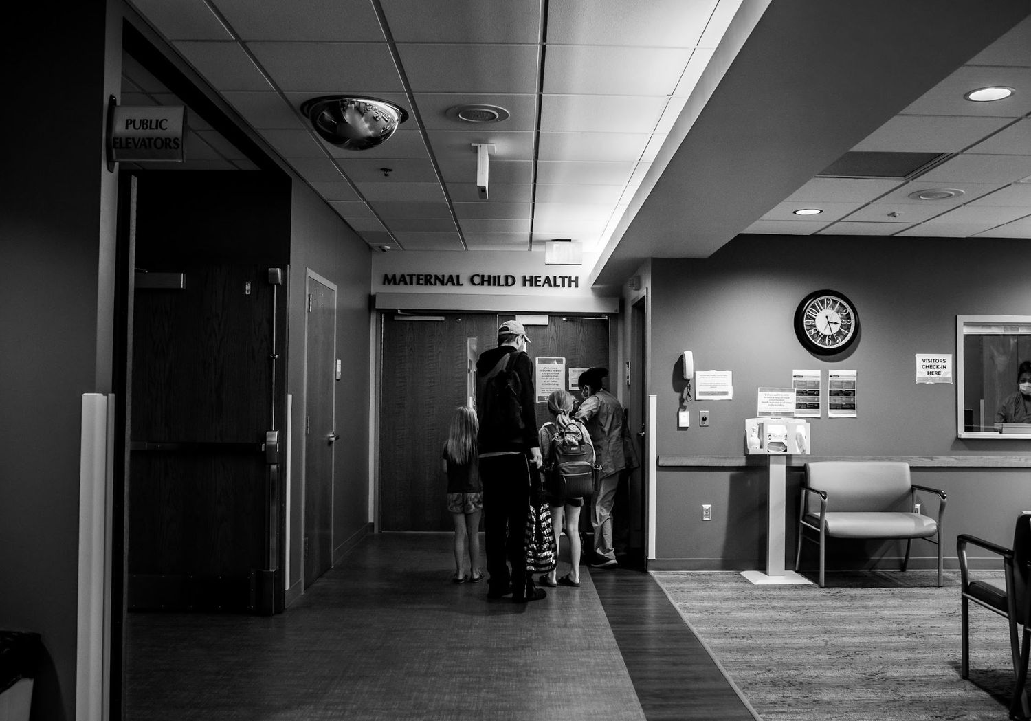 Hospital hallway with people standing near labor and delivery unit entrance.