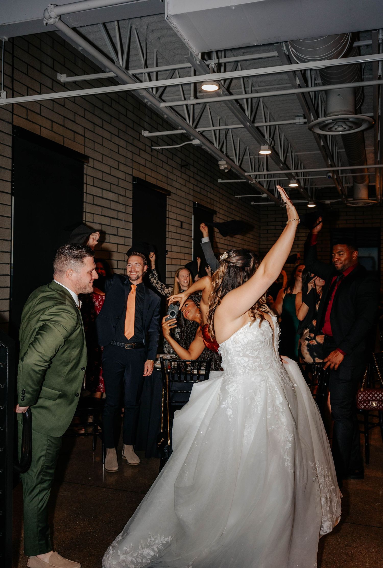 Bride and groom share a first look moment holding hands in a warmly lit industrial wedding venue with string lights.