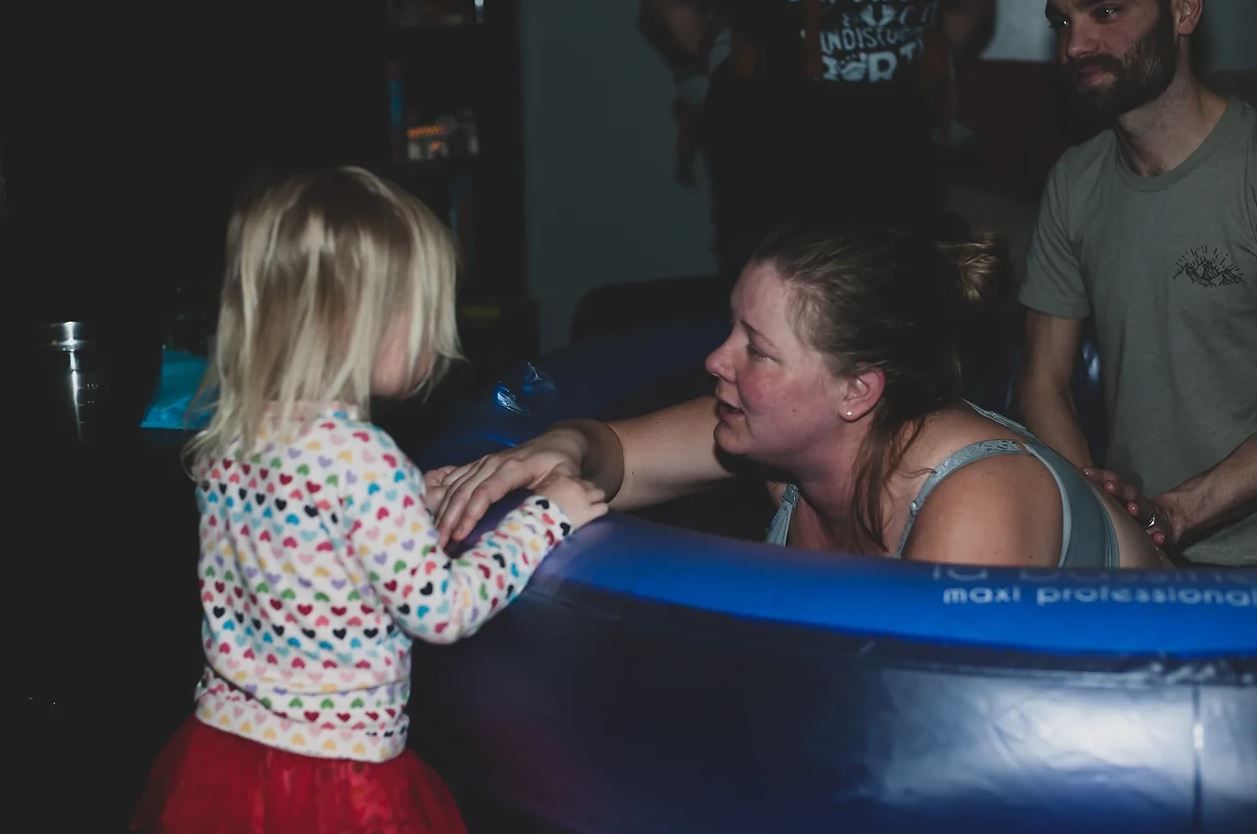 A birthing moment captured in a blue inflatable pool with supportive attendants.