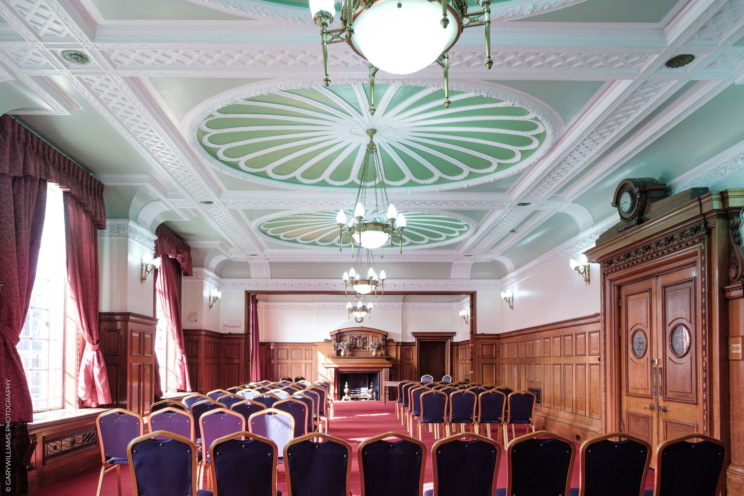 Elegant conference room with ornate green ceiling medallion, purple chairs, and wooden paneling in a historic building.