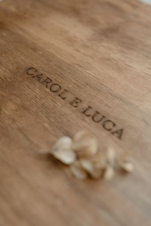Close-up of wooden surface with engraved text 'CAROL B LUCA' and small white flower petals in soft focus.