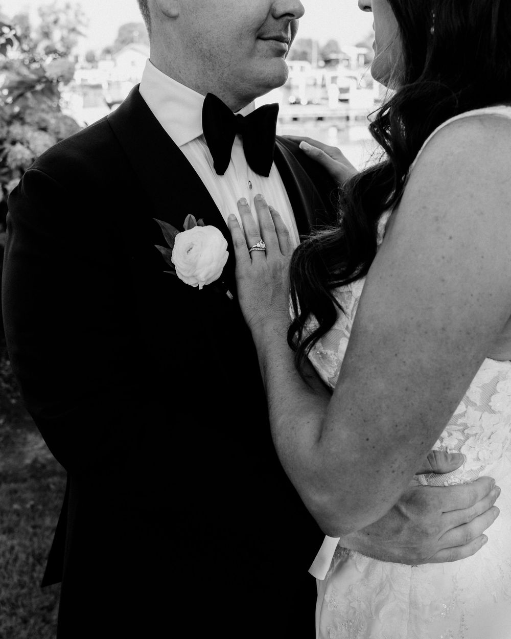 Black and white wedding photo of bride and groom embracing, groom in tuxedo with boutonniere.