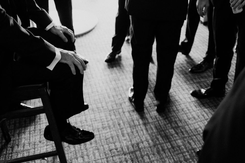 Black and white photo of men in formal suits gathered together, showing legs and hands in elegant attire.