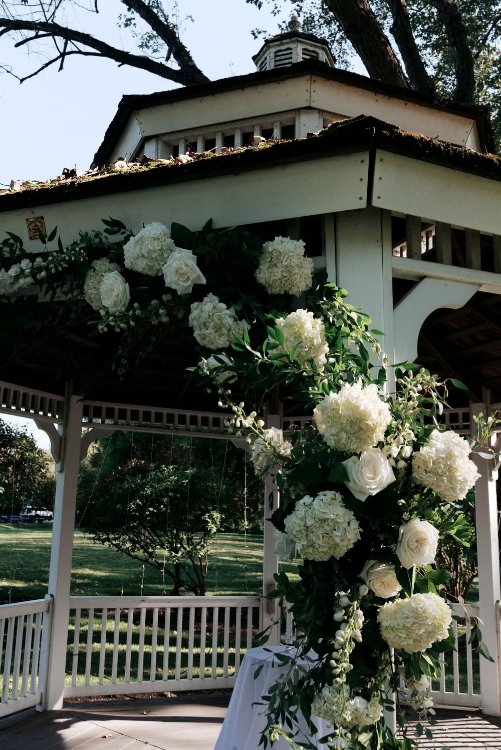 White gazebo adorned with lush floral arrangements of hydrangeas and roses for an elegant outdoor wedding ceremony.