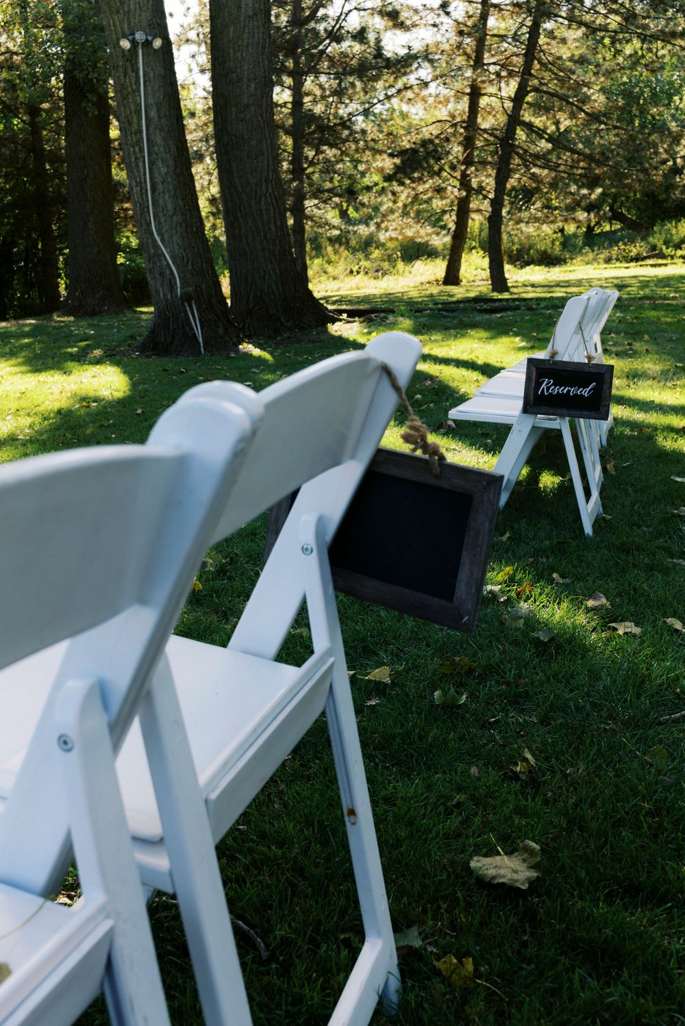 White folding chairs arranged on green grass with a Reserved chalkboard sign at an outdoor wedding ceremony.