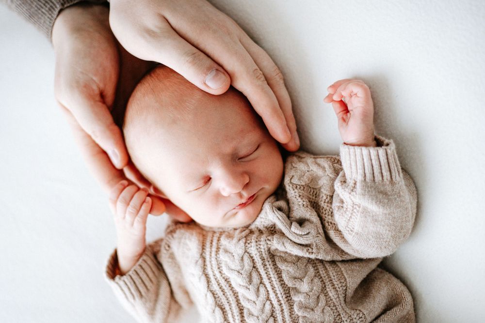 A sleeping newborn baby wearing a cozy knit sweater rests peacefully against a white background.