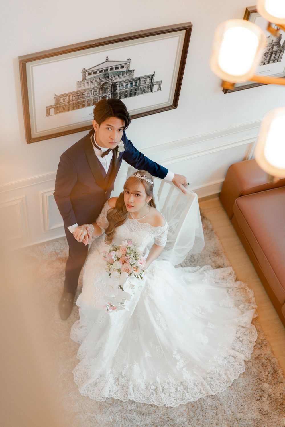 An overhead view of a wedding couple posing in an elegant white room with architectural artwork.
