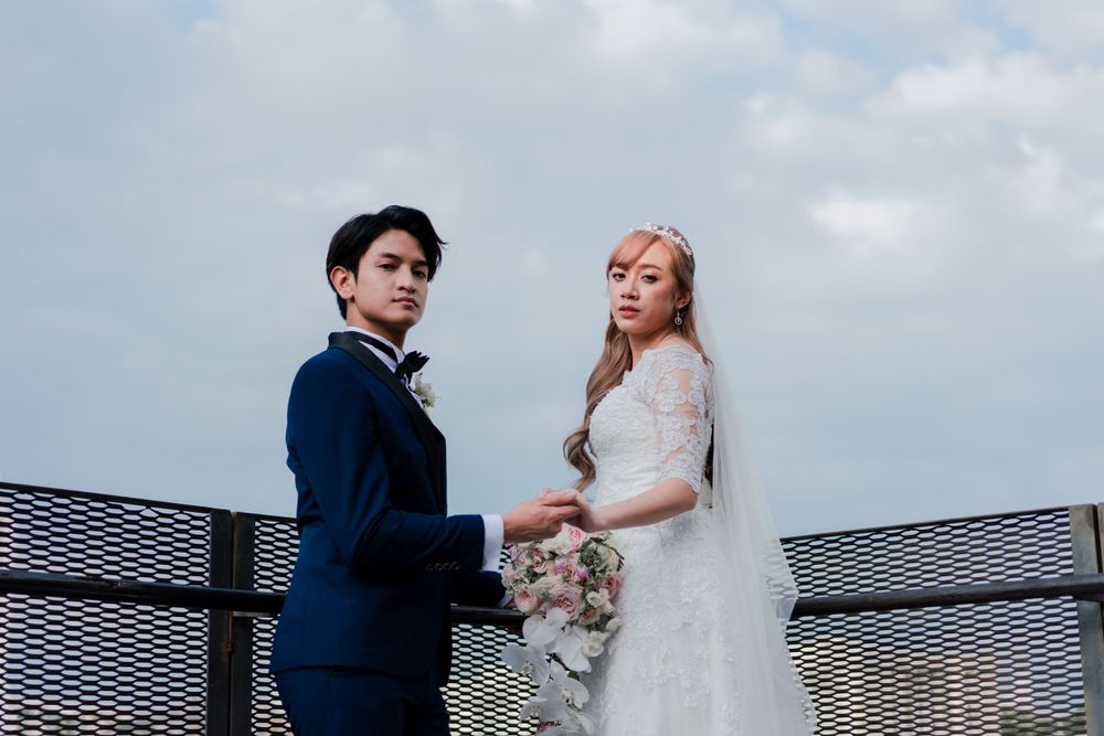 Couple poses on rooftop with modern architecture and cloudy sky backdrop.
