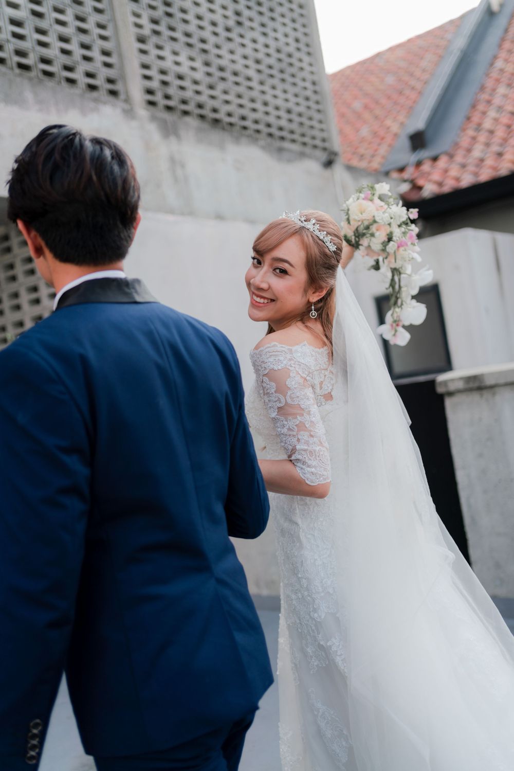 Bride in lace gown looks back with a joyful smile while holding bouquet.