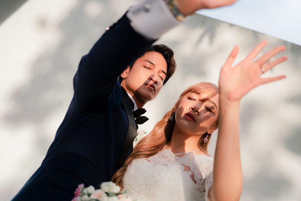 Playful wedding portrait with couple showing dynamic movement against white wall.