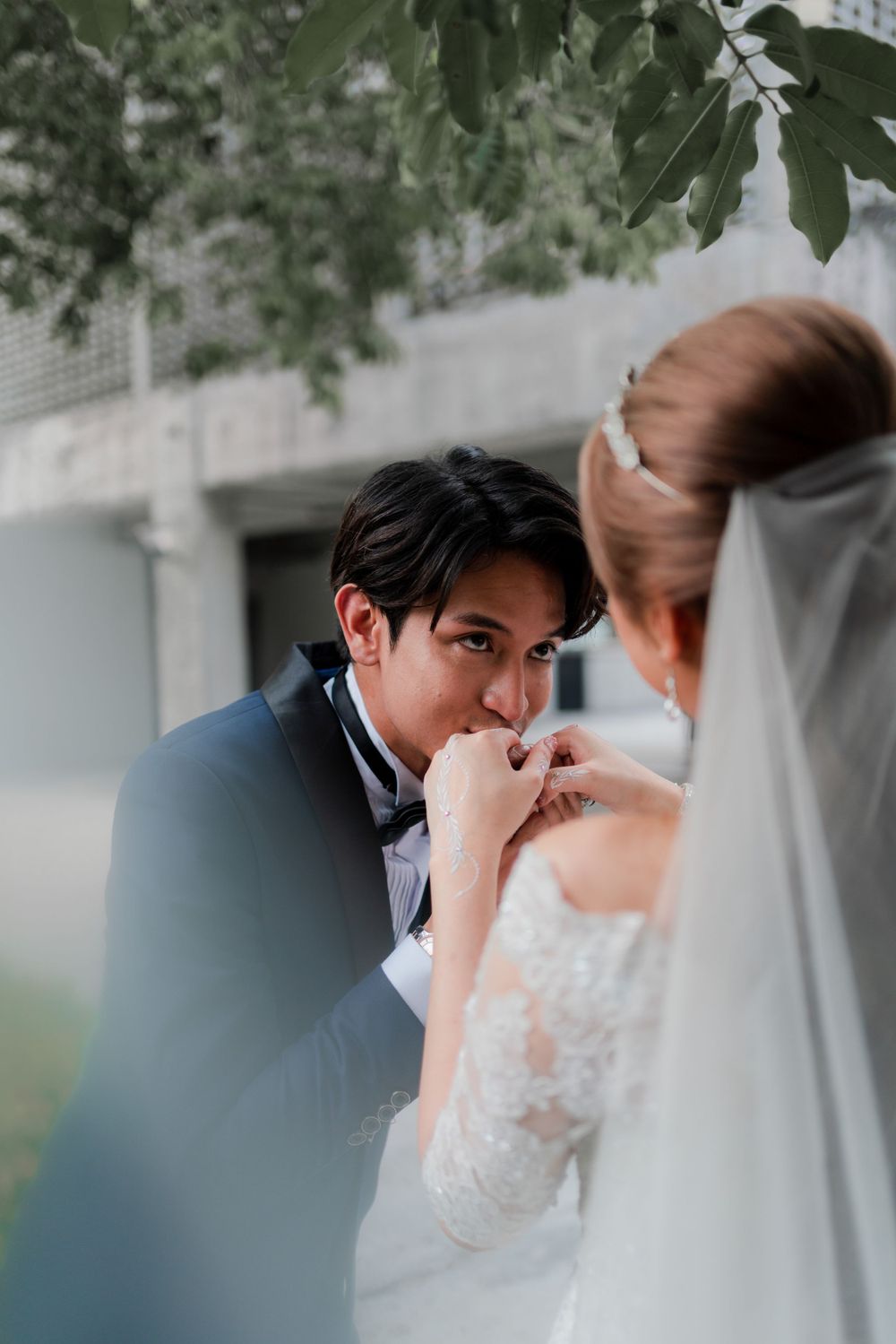 Romantic moment captured through green foliage during outdoor wedding shoot.
