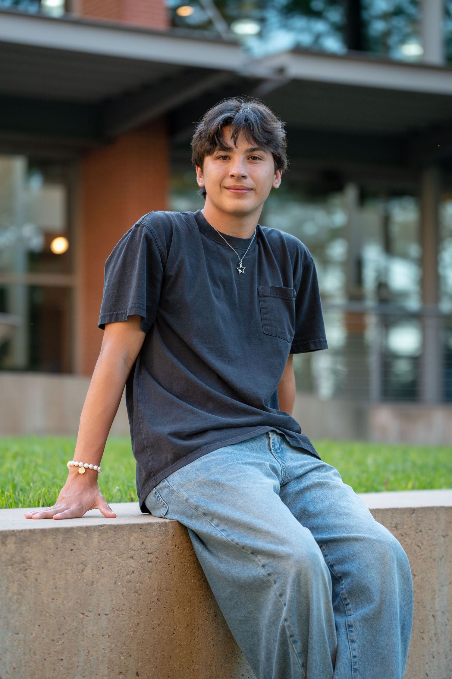 A casual portrait of someone in a dark t-shirt sitting on a concrete ledge outdoors.
